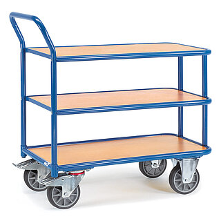 ein blauer FETRA® Magazinwagen aus Stahlrohr mit drei bündig eingelegten Plattformen aus hellem Holz, nach hinten gebogenem Schiebebügel, zwei Bockrollen vorne und zwei Lenkrollen hinten, freigestellt auf weißem Hintergrund