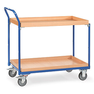 ein blauer FETRA® Tischwagen aus Stahlrohr und Profilstahl mit zwei großflächigen Etagen, nach hinten gebogenem Schiebebügel, hellen aufgesetzten Holzrahmenkästen oben und unten, zwei Bockrollen vorne und zwei feststellbaren Lenkrollen hinten, freigestellt auf weißem Hintergrund