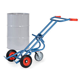 eine blaue FETRA® Karre aus Stahlrohr für den Transport von Fässern, mit zwei Rädern mit Vollgummi-Bereifung auf roten Felgen, roten Handgriffen und geschwungener Stütze für Schräglage in Ruheposition mit zusätzlichem dritten drehbaren Stützrad, dahinter ein graues 200 Liter Fass aus Metall, freigestellt auf weißem Hintergrund