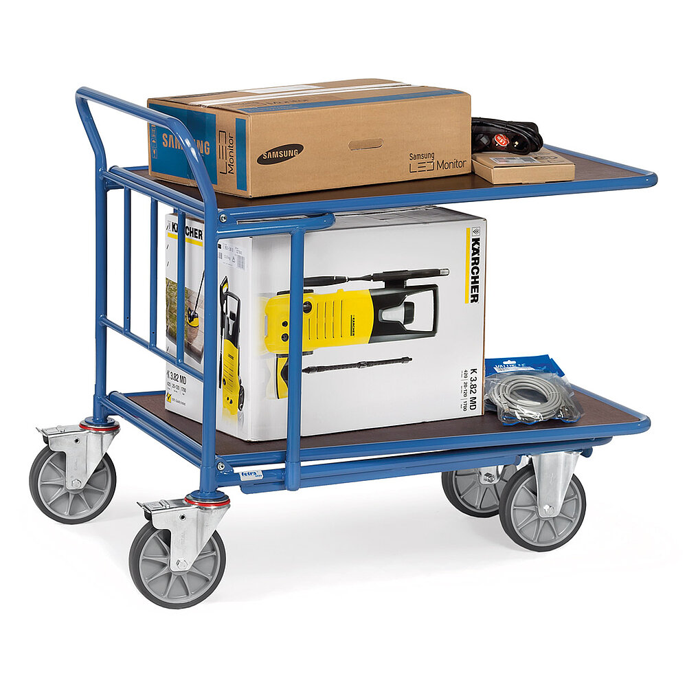 ein blauer FETRA® Plattformwagen mit Schiebebügel aus Stahlrohr, zwei Bockrollen vorne, zwei feststellbaren Lenkrollen hinten, zwei braunen Ladeplattformen aus Holz und beladen mit Konsumartikel-Kartons aus dem Baumarkt-Bereich, freigestellt auf weißem Hintergrund