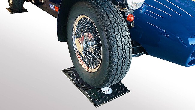 ein schwarzer konvexer TyreGuard® Reifenschoner aus hochfestem Kunststoff mit Antirutschmatte unter einem blauen historischen Sportwagen