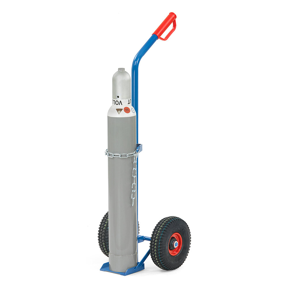 eine blaue FETRA® Karre aus Stahlrohr für Stahlflaschentransport mit dreiseitig umrandeter Ladeschaufel, Luftbereifung auf roten Felgen, rotem Handgriff auf nach hinten geknicktem Schiebebügel, Kettensicherung für die Gasflasche und beladen mit einer schlanken grauen Gasflasche, freigestellt auf weißem Hintergrund