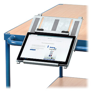 ein angeschaltetes Tablet in einem FETRA® Tablethalter aus verzinktem Stahlblech, schräg montiert am Schiebebügel eines blauen FETRA® Tischwagens mit heller Tischplatte aus Holz, freigestellt auf weißem Hintergrund