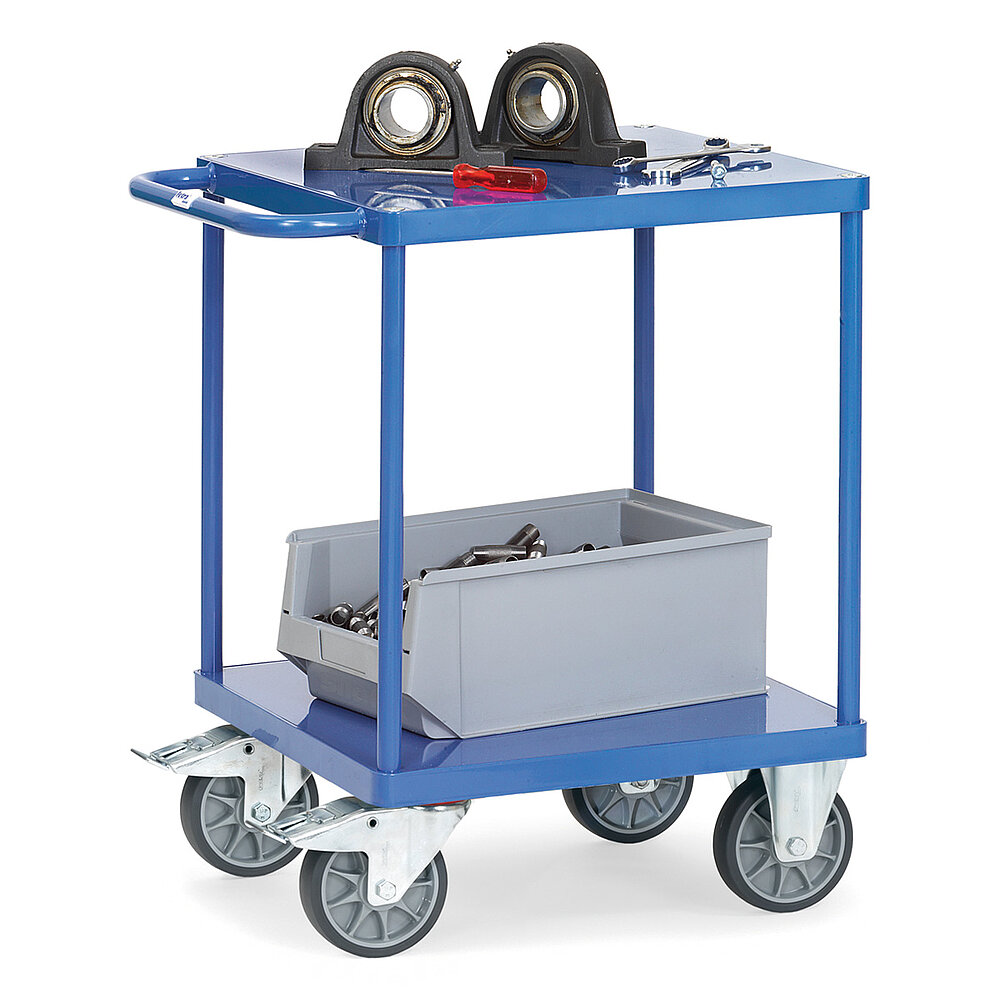 ein quadratischer blauer FETRA® Tischwagen aus Stahlrohr und Profilstahl mit zwei Etagen, Schiebebügel, bündigen Stahlblechplattformen, zwei Bockrollen vorne, zwei feststellbaren Lenkrollen hinten und beladen mit einer grauen Kunststoffkiste und Rundlagern, freigestellt auf weißem Hintergrund