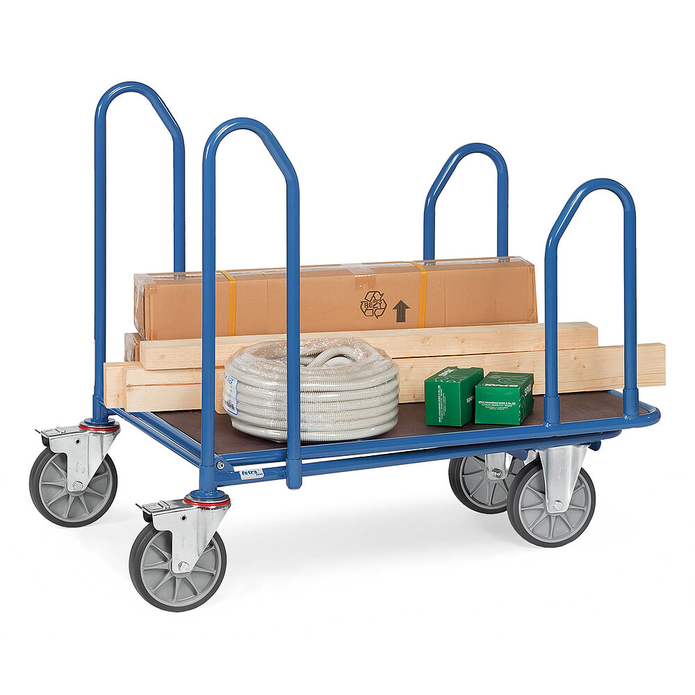 ein blauer FETRA® Plattformwagen mit vier seitlich angebrachten gebogenen Haltebügeln aus Stahlrohr, zwei Bockrollen vorne, zwei feststellbaren Lenkrollen hinten, brauner Ladeplattform aus Holz und beladen mit verschiedenen Baumarktartikeln, freigestellt auf weißem Hintergrund
