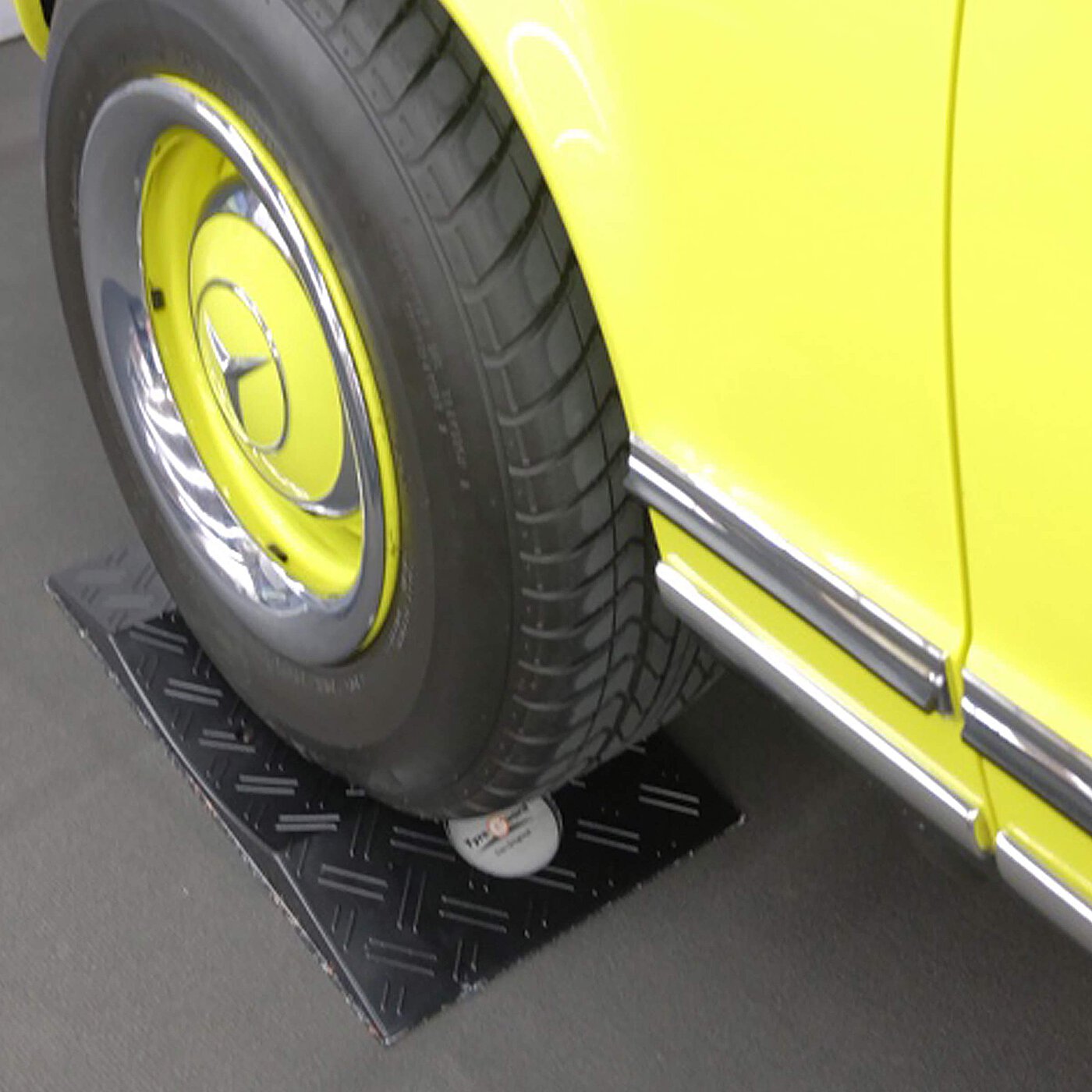 ein schwarzer konkaver TyreGuard® Reifenschoner aus hochfestem Kunststoff unter einem gelben Youngtimer