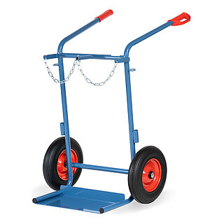 eine breite blaue FETRA® Karre aus Stahlrohr für Stahlflaschentransport mit dreiseitig umrandeter Ladeschaufel, Vollgummi-Bereifung auf roten Felgen, roten Handgriffen auf nach hinten geknickten Schiebebügeln und Kettensicherung für zwei stehend platzierte breite Gasflaschen, freigestellt auf weißem Hintergrund