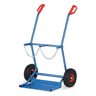 eine breite blaue FETRA® Karre aus Stahlrohr für Stahlflaschentransport mit dreiseitig umrandeter Ladeschaufel, Luftbereifung auf roten Felgen, roten Handgriffen und Kettensicherung für zwei stehend platzierte breite Gasflaschen, freigestellt auf weißem Hintergrund