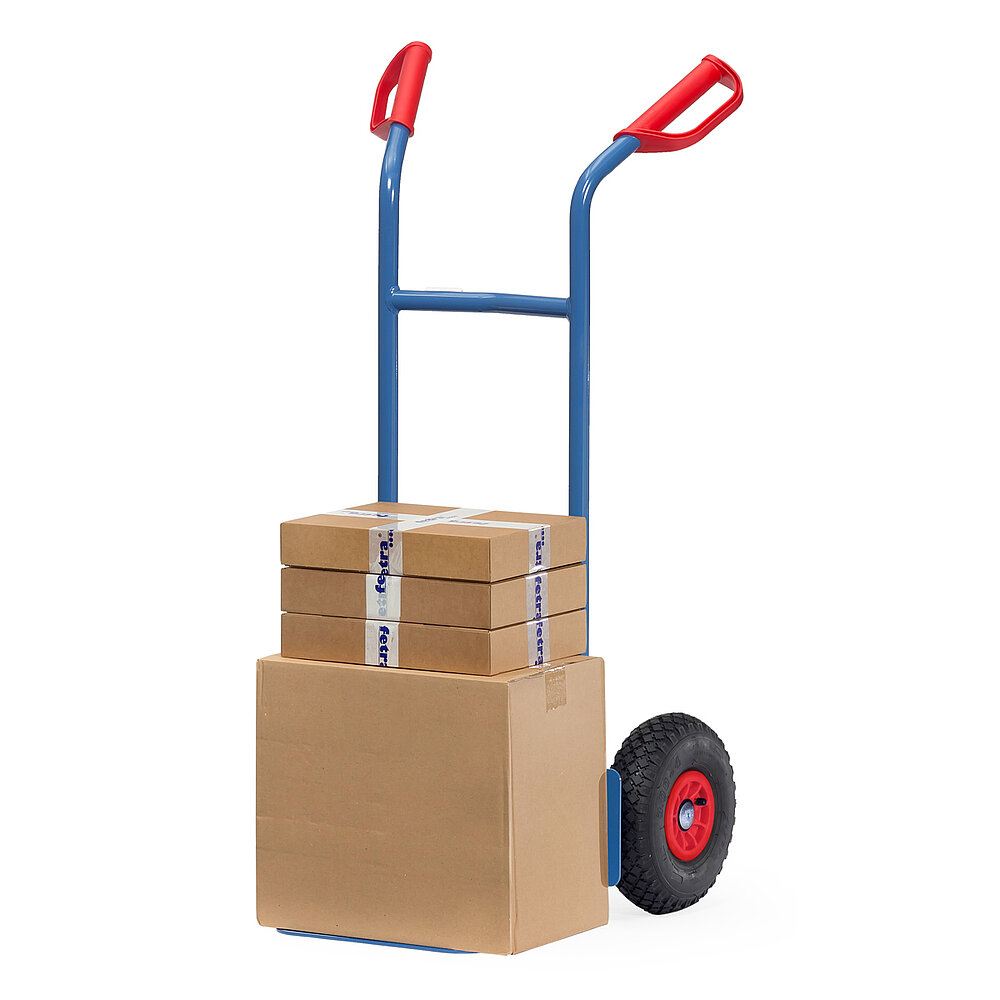 eine blaue FETRA® Stapelkarre aus Stahlrohr mit Luftbereifung, roten Handgriffen und beladen mit braunen Pappkartons auf weißem Hintergrund