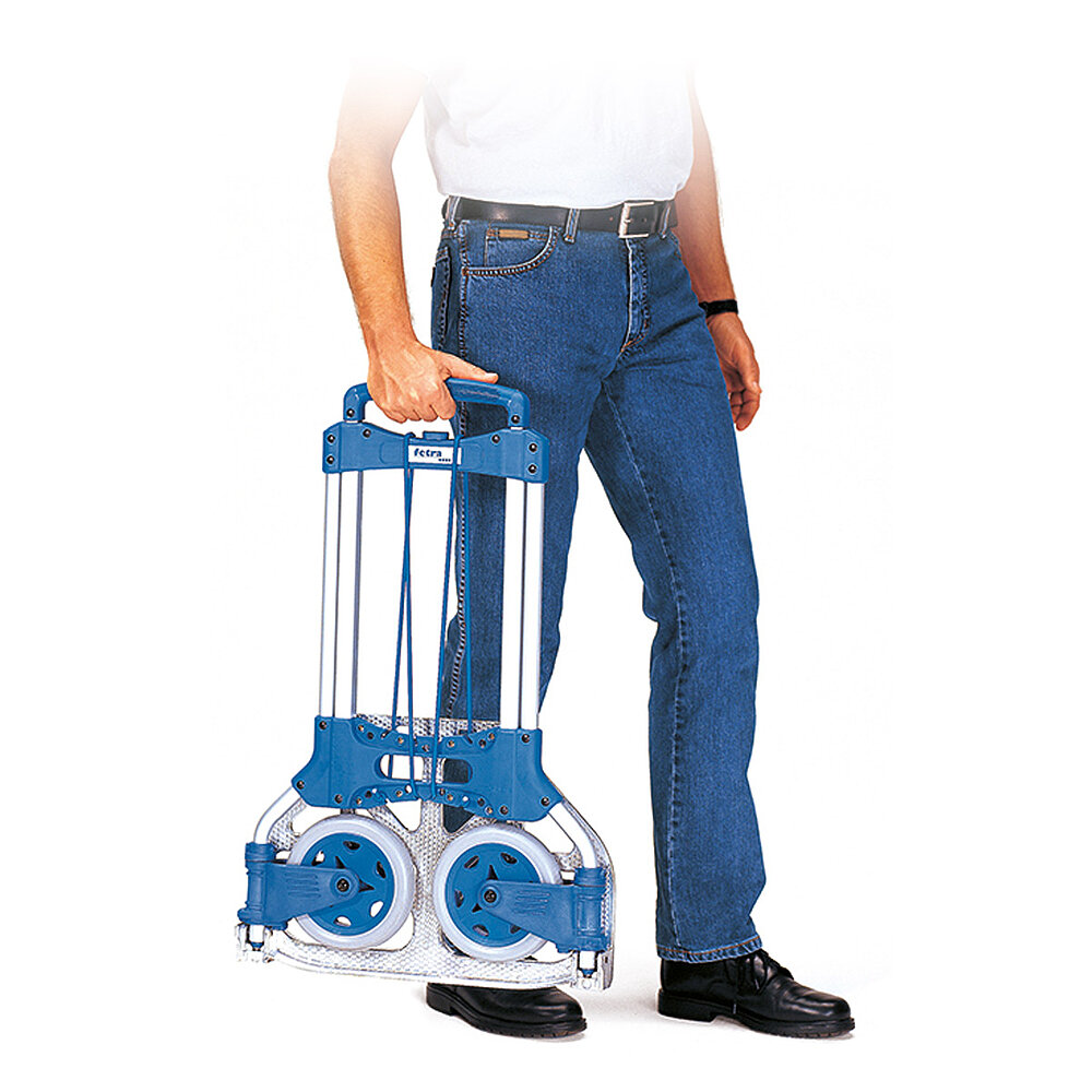 Anwendungsdetail eines zusammengeklappten FETRA® Paketrollers aus silbrigem Aluminiumrohr mit blauem Kunststoffgriff und elastischer Gummisicherungsschnur, getragen von einem Mann in blauer Jeans auf weißem Hintergrund