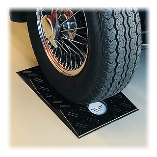 ein schwarzer konvexer TyreGuard® Reifenschoner aus hochfestem Kunststoff mit Antirutschmatte unter einem Reifen auf klassischer verchromter Speichenfelge