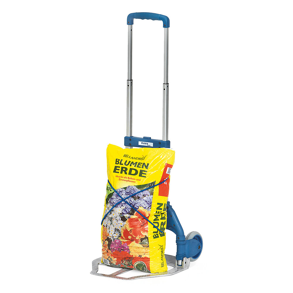 ein zusammenklappbarer FETRA® Paketroller aus silbrigem Aluminiumrohr mit blauem Kunststoffgriff, elastischer Gummisicherungsschnur und beladen mit einem gelben Sack Blumenerde auf weißem Hintergrund
