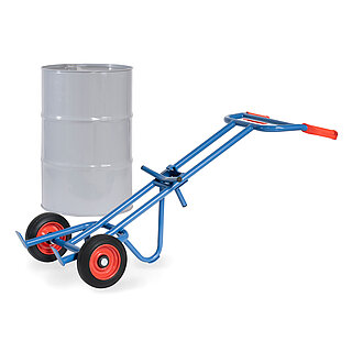 eine blaue FETRA® Karre aus Stahlrohr für den Transport von Fässern, mit zwei Rädern mit Vollgummi-Bereifung auf roten Felgen, roten Handgriffen und geschwungener Stütze für Schräglage in Ruheposition, dahinter ein graues 200 Liter Fass aus Metall, freigestellt auf weißem Hintergrund