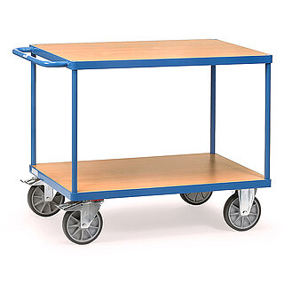 ein blauer FETRA® Tischwagen aus Stahlrohr und Profilstahl mit zwei Etagen, Schiebebügel, hellen Holzeinlegeböden, zwei Bockrollen vorne und zwei feststellbaren Lenkrollen hinten, freigestellt auf weißem Hintergrund