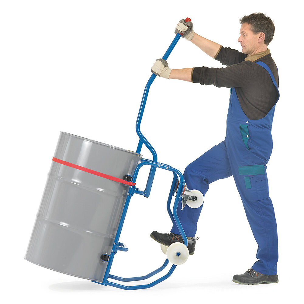 ein Arbeiter mit einem blauen FETRA® Fasskipper aus Stahlrohr mit zwei feststehenden Rädern und zwei feststellbaren Lenkrollen aus weißem Polyamid, beladen mit einem grauen 200 Liter Fass aus Metall, gesichert mit einem roten Spanngurt, halb gekippt mittells eingesteckter Hebelstange, freigestellt auf weißem Hintergrund