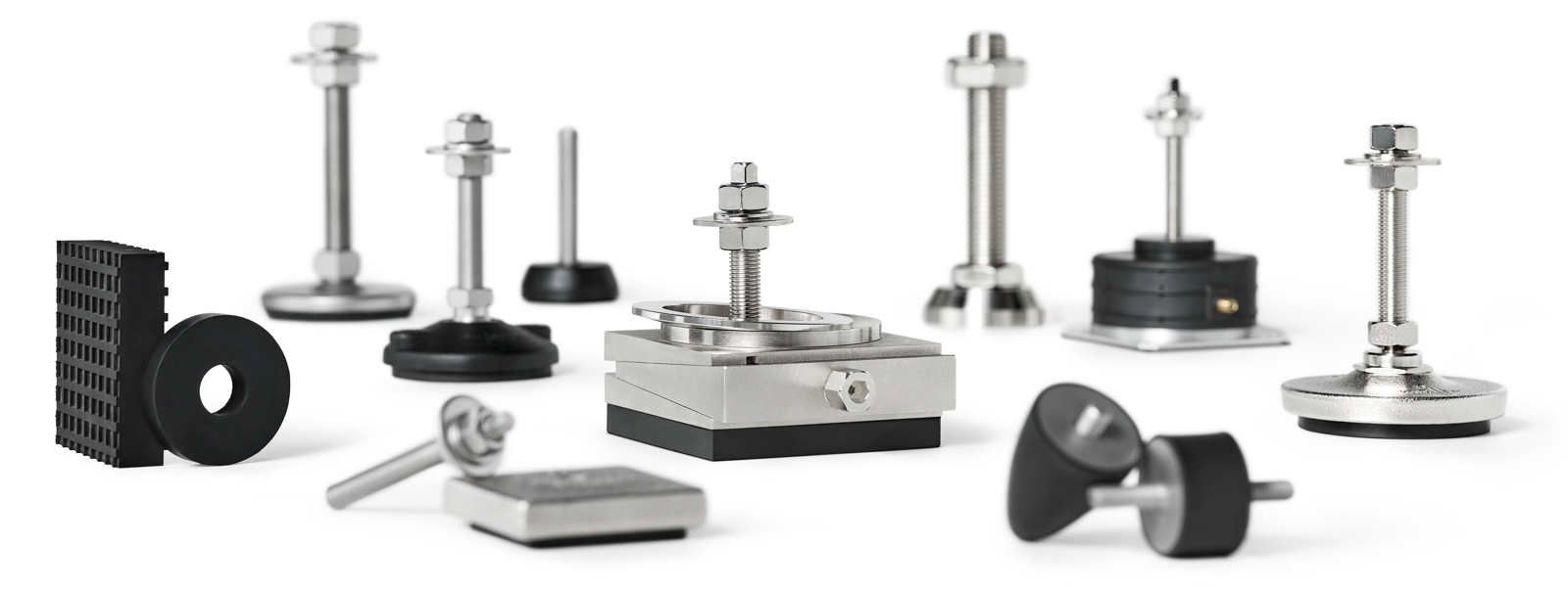 ein silberner Maschinen-Keilschuh mit Kalotte und Schraube, zwei schwarze Gummi-Metall-Elemente, ein passiv isolierendes Luftfeder-Element, schwarze Elastomere und diverse weitere Nivellierelemente aus Stahl und Guss, alle zur Maschinenaufstellung und Schwingungsdämpfung, freigestellt auf weißem Hintergrund